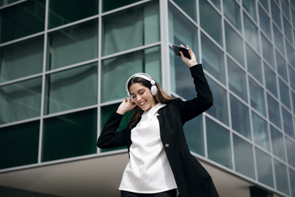 a woman wearing headphones listening to binaural beats and dancing with her phone